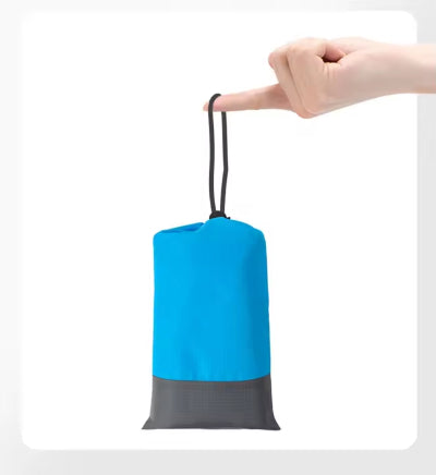 Ruka drzi spakovanu prostirku za plazu u kompaktnu torbicu sa vezicom, istice prenosivost i lako skladistenje.