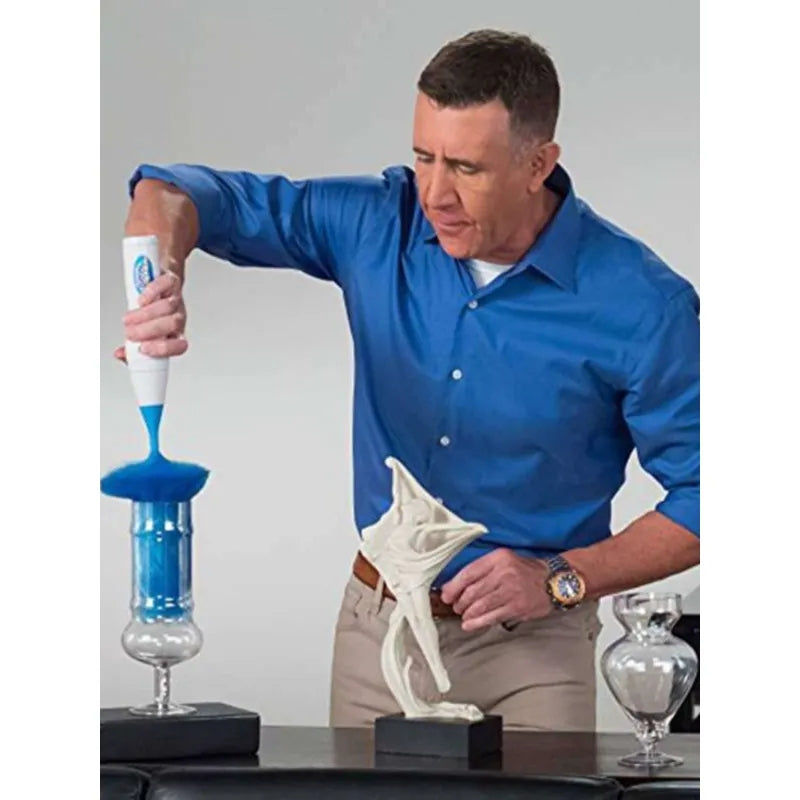 Muskarac bele puti, verovatno srednjih godina, koristi elektricnu cetku za prasinu ActiDust sa plavom cetkom za ciscenje staklenog ukrasnog predmeta na crnom postolju. Na stolu se nalazi i drugi stakleni predmet.