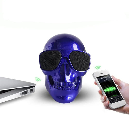 Bluetooth zvučnik u obliku plave lobanje sa svetlećim očima, bežično povezan sa pametnim telefonom koji prikazuje vizualizaciju zvuka i laptopom. Zeleni simboli označavaju aktivnu Bluetooth vezu.