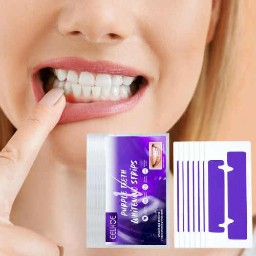Prikaz žene koja prstom pokazuje na svoje bele zube. U prvom planu su pakovanje Eelhoe ljubičastih trakica za izbeljivanje zuba i otvoreno pakovanje sa trakicama i aplikatorom.