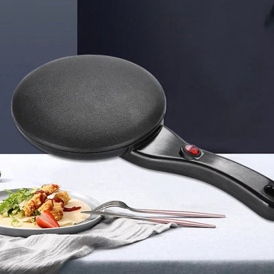 moderna crna elektricna palacinkara na stolu pored tanjira sa ukusnim desertom spremna za upotrebu u svakoj kuhinji