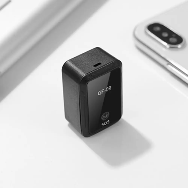 Crni GF-09 mini GPS tracker pored bele mobilne telefonske slusalice na beloj povrsini. Na trackeru pise GF-09 i SOS.