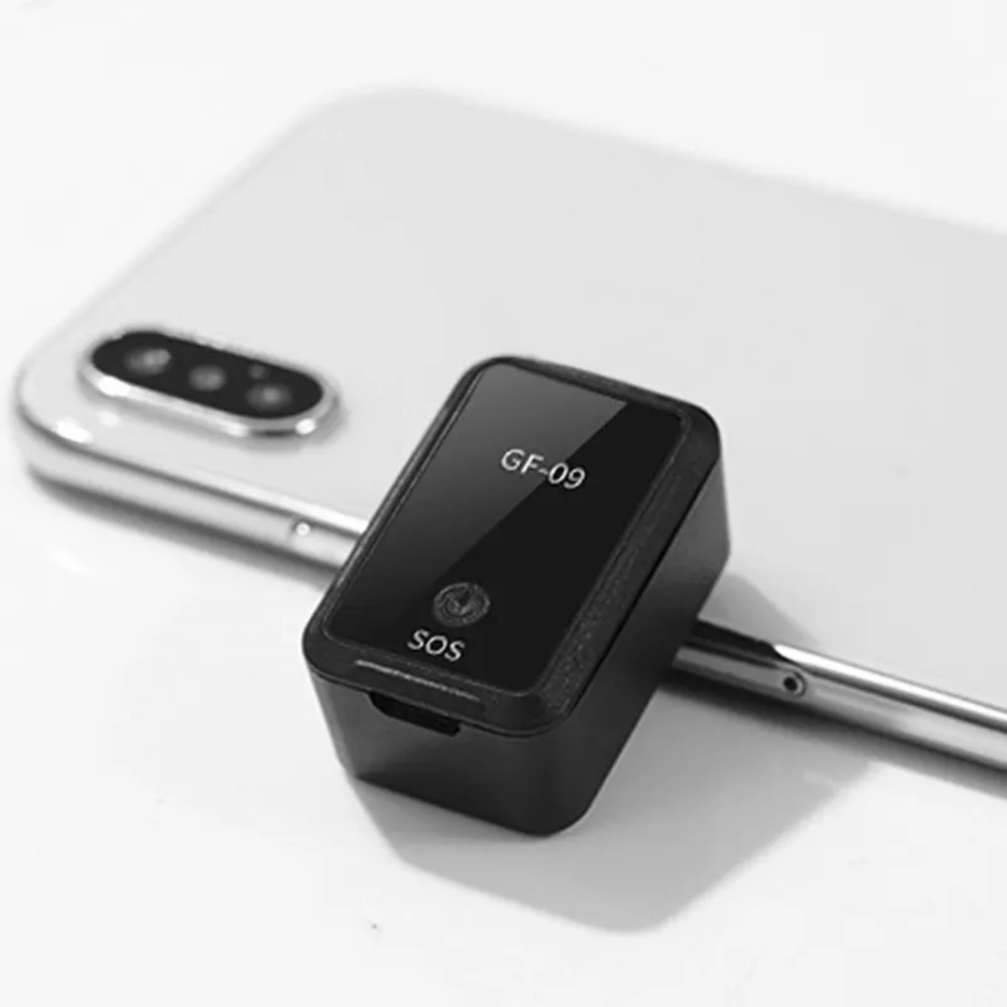 Crni GF-09 mini GPS tracker pored bele mobilne telefonske slusalice. Na trackeru pise GF-09 i SOS.