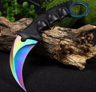 Karambit noz sa secivom duginih boja i crnom drskom, naslonjen na drveni panj, pogodan za kolekcionare i ljubitelje CS:GO igrice.