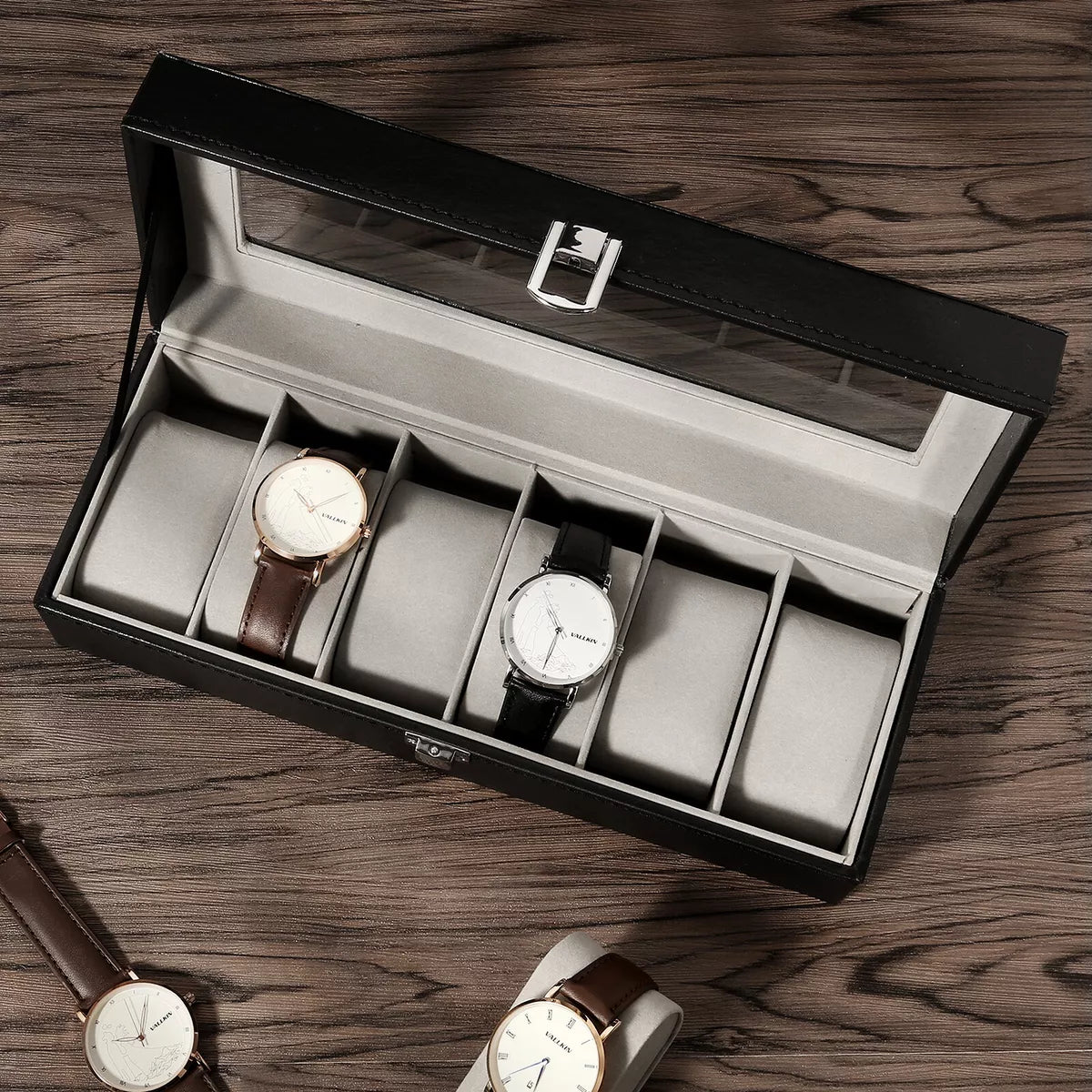 Otvorena crna kutija za ručne satove sa šest pregrada obloženih sivim materijalom. Elegantna kutija sa providnim poklopcem, idealna za organizovanje i čuvanje kolekcije satova.