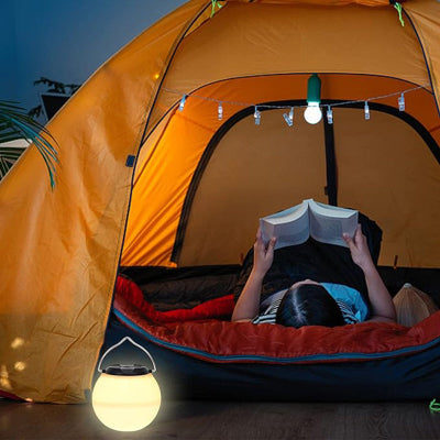 Lampa u upotrebi unutar satora, prikazuje coveka koji je koristi, savrsena za kampovanje i aktivnosti u prirodi.