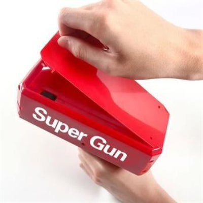 Ruke pune igracku Super Gun laznom novcanicom. Prikazuje jednostavan proces punjenja pistolja novcanicama kako bi bio spreman za upotrebu.