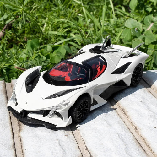 Model belog sportskog automobila Apollo Evo sa crnim detaljima i crvenom unutrasnjosti postavljen je na svetloj kamenoj povrsini. U pozadini je zeleno lisce i trava, sto stvara kontrast sa cistom belom bojom automobila.