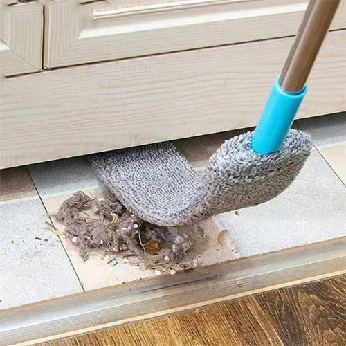 Detaljan snimak prikazuje fleksibilni sivi cistac prasine sa svetloplavom drskom kako cisti prljavstinu i prasinu ispod svetlog ormarica. Prasina se nakupila na svetloj plocici pored drvenog poda.