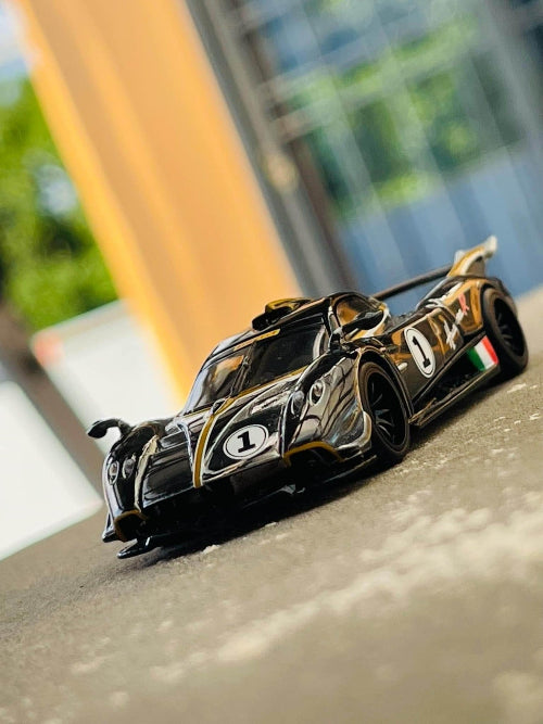 Model crnog Pagani Huayra R automobila sa zlatnim detaljima i brojem jedan na vratima postavljen je na sivoj povrsini.