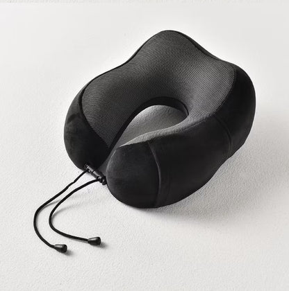 Fotografija prikazuje crni jastuk za vrat sa sivim prugastim detaljima u obliku slova "U". Jastuk leži na beloj površini, a vide se i crne vezice sa plastičnim krajevima.