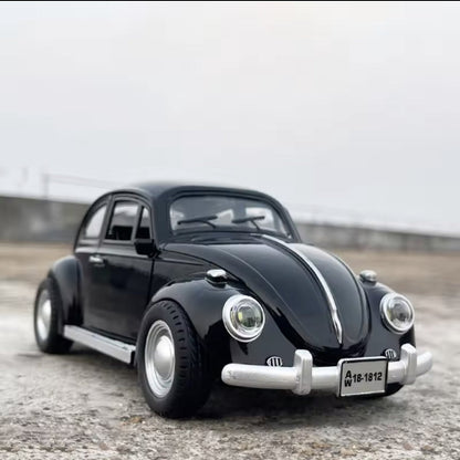Model crnog Volkswagen Beetle automobila stoji na sivoj betonskoj povrsini. U pozadini je svetlo sivo nebo. Na prednjoj strani automobila vidi se registarska tablica sa natpisom "A 18-1812".