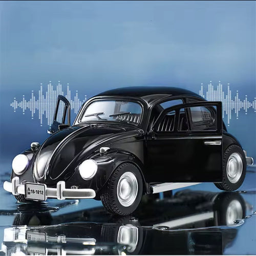 Model crnog Volkswagen Beetle automobila sa otvorenim prednjim vratima i upaljenim prednjim svetlima stoji na crnoj reflektujucoj povrsini. U pozadini je plava pozadina sa belim grafickim prikazima zvucnih talasa. Na prednjoj strani automobila vidi se registarska tablica sa natpisom "A 18-1812".