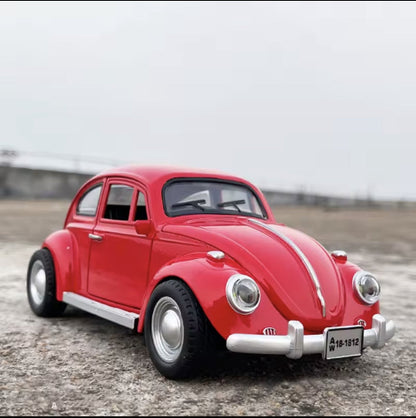 Model crvenog Volkswagen Beetle automobila stoji na sivoj betonskoj povrsini. U pozadini je svetlo sivo nebo. Na prednjoj strani automobila vidi se registarska tablica sa natpisom "A 18-1812".
