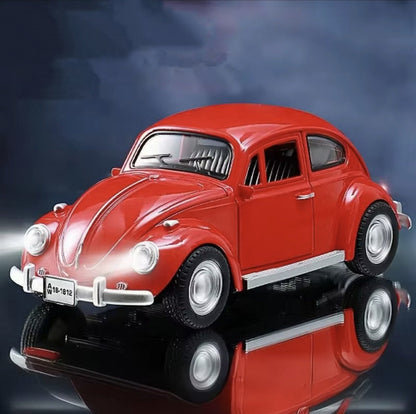 Model crvenog Volkswagen Beetle automobila sa upaljenim prednjim svetlima stoji na crnoj reflektujucoj povrsini. U pozadini je tamno plavo nebo sa oblacima. Na prednjoj strani automobila vidi se registarska tablica sa natpisom "A 18-1812".
