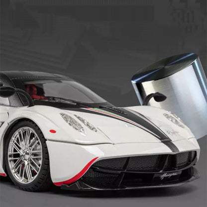 Krupni plan prednjeg dela belog modela automobila Pagani Huayra sa crnim i zelenim prugama na haubi. Fokus je na prednjim svetlima, tocku sa hromiranim felnama i delu otvorenih vrata sa retrovizorom. 