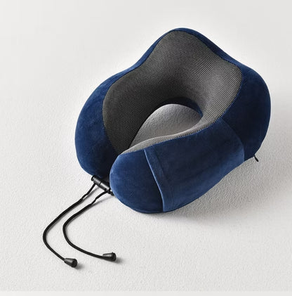 Fotografija prikazuje plavi jastuk za vrat sa svetlosivim prugastim detaljima u obliku slova "U". Jastuk leži na beloj površini, a vide se i crne vezice sa plastičnim krajevima.