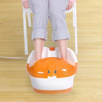 Električna kadica za stopala u beloj i narandžastoj boji, napunjena vodom, sa stopalima osobe koja sedi na beloj stolici iznad nje. Kadica ima kontrolni panel sa dugmićima i kabl za napajanje.