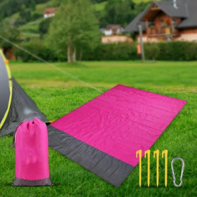 Roze-siva prostirka rasirena na travi, pogodna za piknik, suncanje ili relaksaciju u basti i prirodi. Zivahna boja.