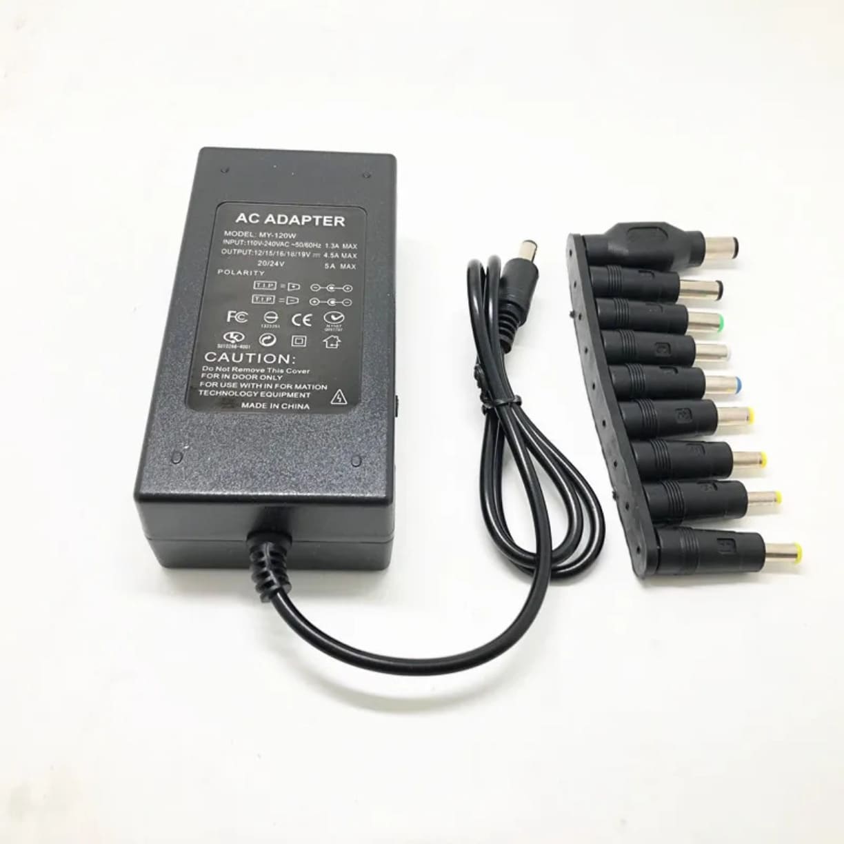 Crni adapter za laptop prikazan sa donje strane sa tekstom tehnicke specifikacije i povezanim kablom pored niza konektora
