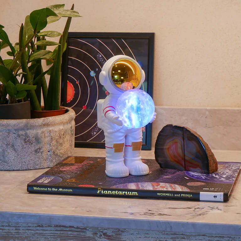 Astronaut lampa projektor na stolu pored telefona stvara sferno osvetljenje u sobi