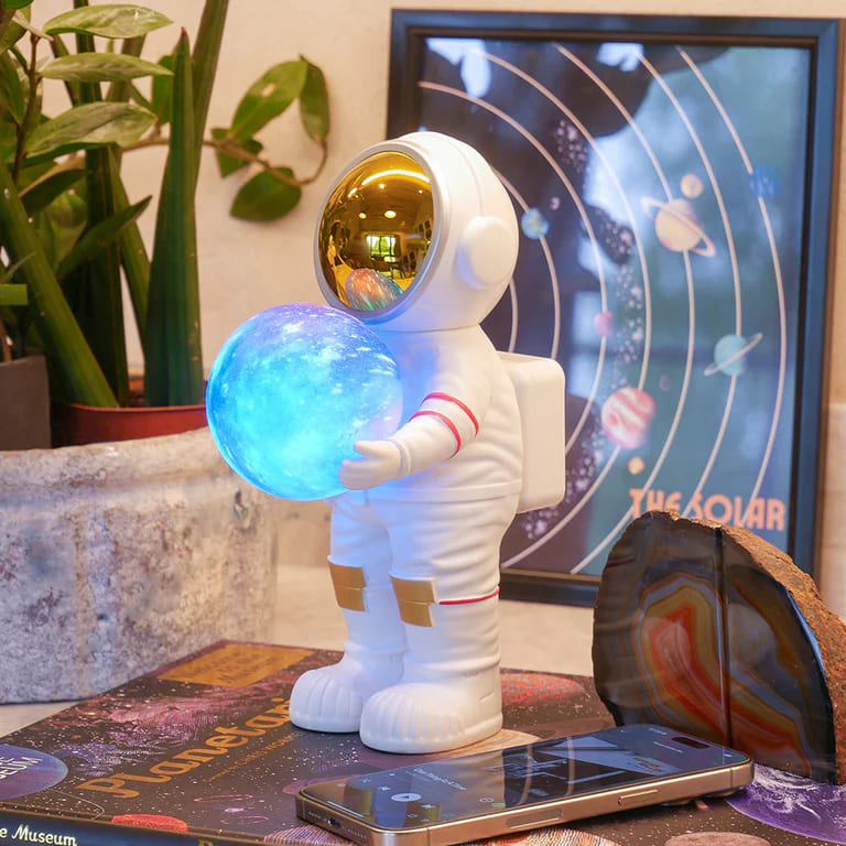 Beli astronaut figura koja drzi svetlecu galaksija kuglu i pusta muziku preko bluetooth-a