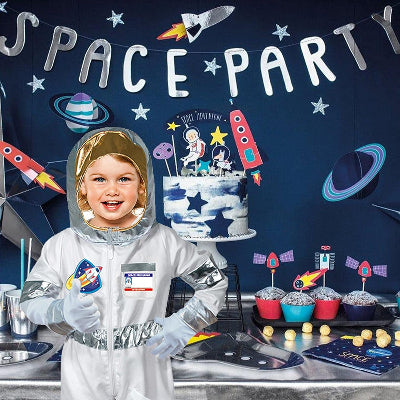 Dete u kostimu astronauta na tematskoj rodjendanskoj proslavi. Dekoracija sa motivima svemira, raketa i zvezda.
