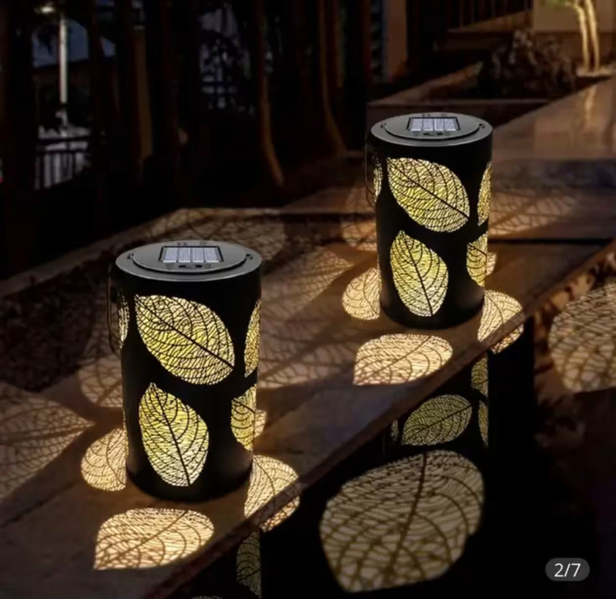 Dve solarne LED lampe sa motivom listova koje osvetljavaju terasu dekorativnim toplim svetlom i prave efektne senke.