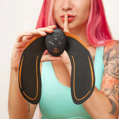 Zena drzi EMS stimulator misica gluteusa u ruci, uredjaj sa kontrolama za elektrostimulaciju i toniranje misica.