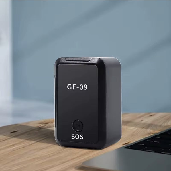 Crni GF-09 mini GPS tracker na drvenom stolu, pored laptopa. Na trackeru pise GF-09 i SOS.