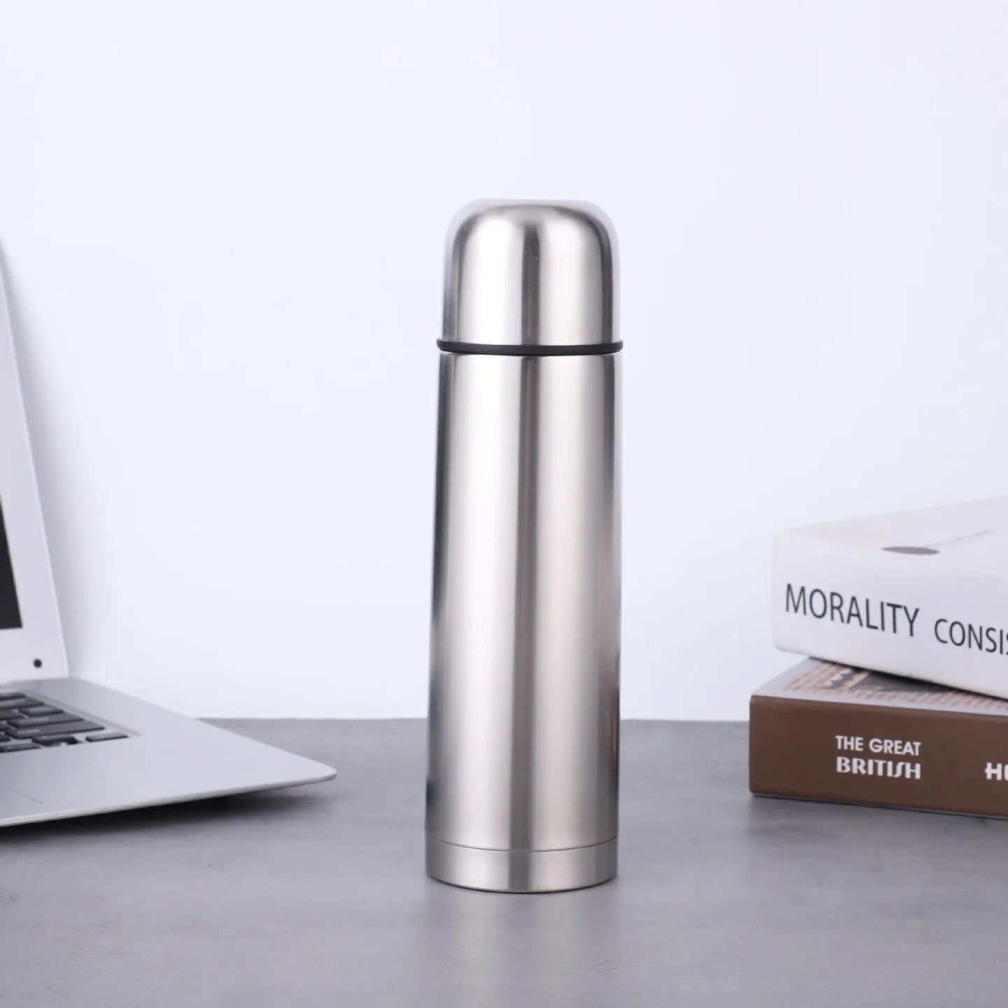 Inoksni termos na stolu pored laptopa i knjiga