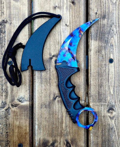 Karambit noz sa dugino obojenim secivom i tamnom drskom. Prikazan na drvenoj povrsini.