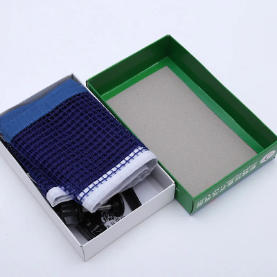 otvorena kutija seta za stoni tenis u kojoj se nalaze plava mrezica i crni metalni nosaci spremno za montazu