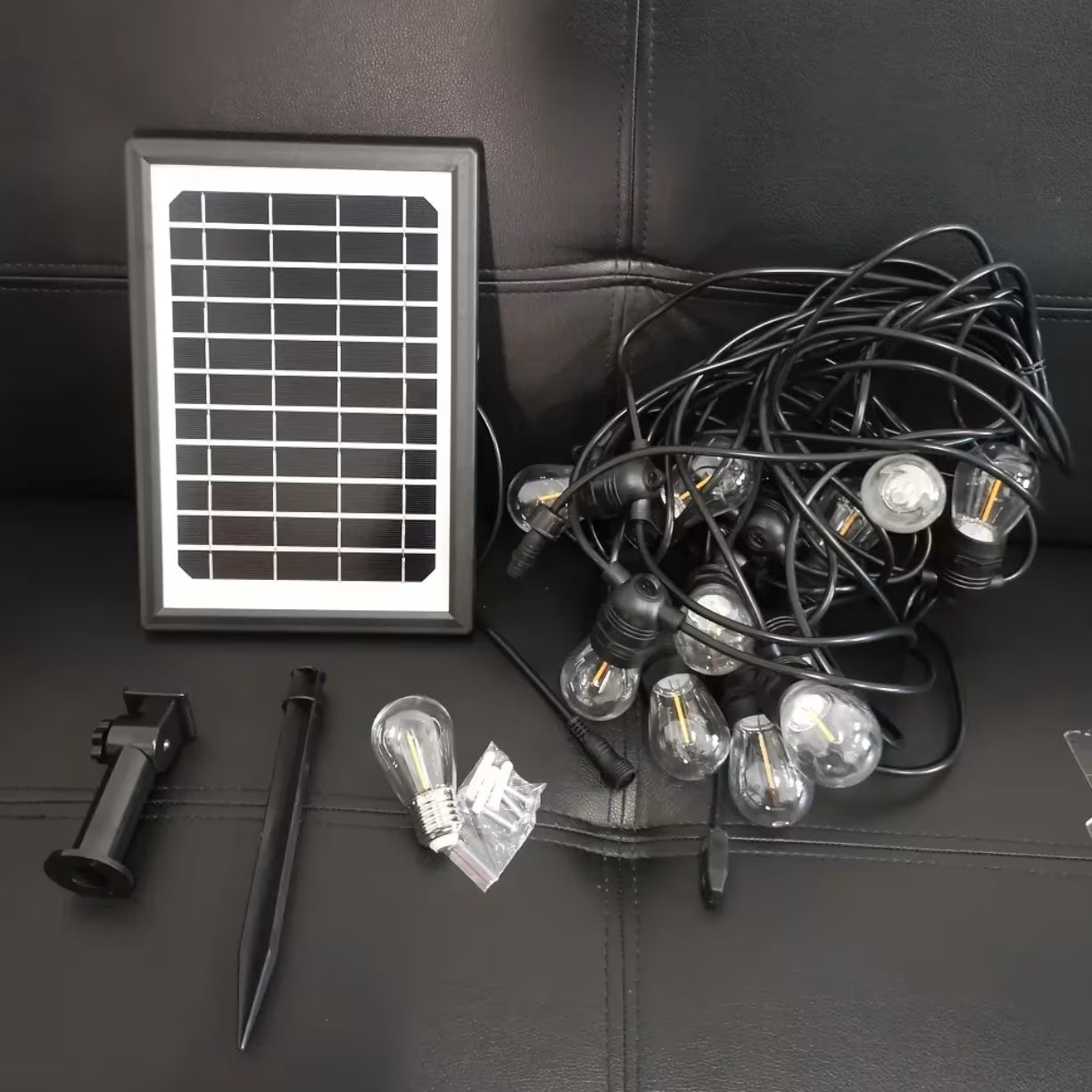 Prikaz svih delova u pakovanju koji ukljucuje urolan crni kabl sa sijalicama solarni panel ubodni nosac i tiplove
