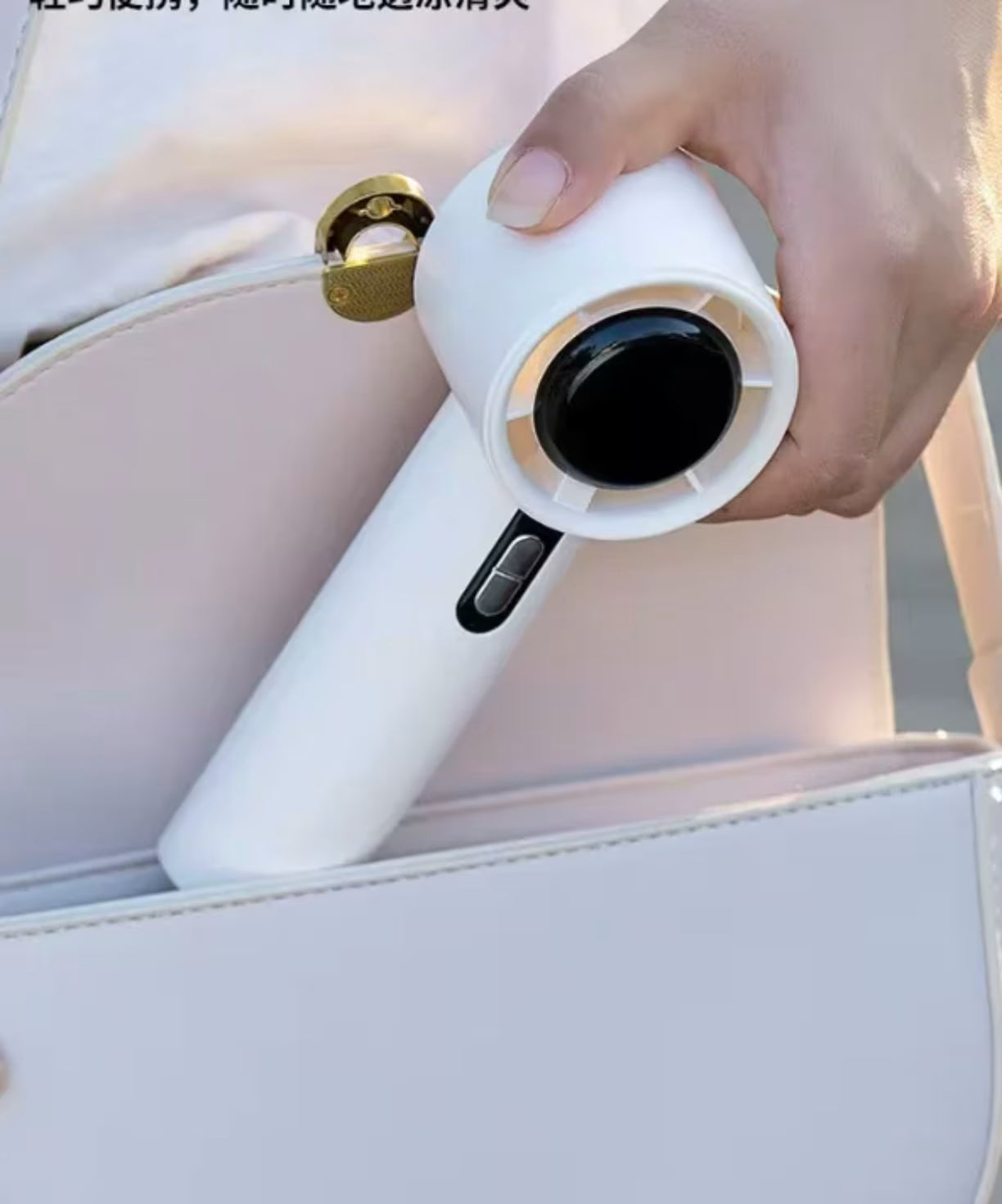 Zenska ruka koja lako pakuje kompaktan beli rucni ventilator u malu belu koznu torbicu kao dokaz prakticnosti za nosenje