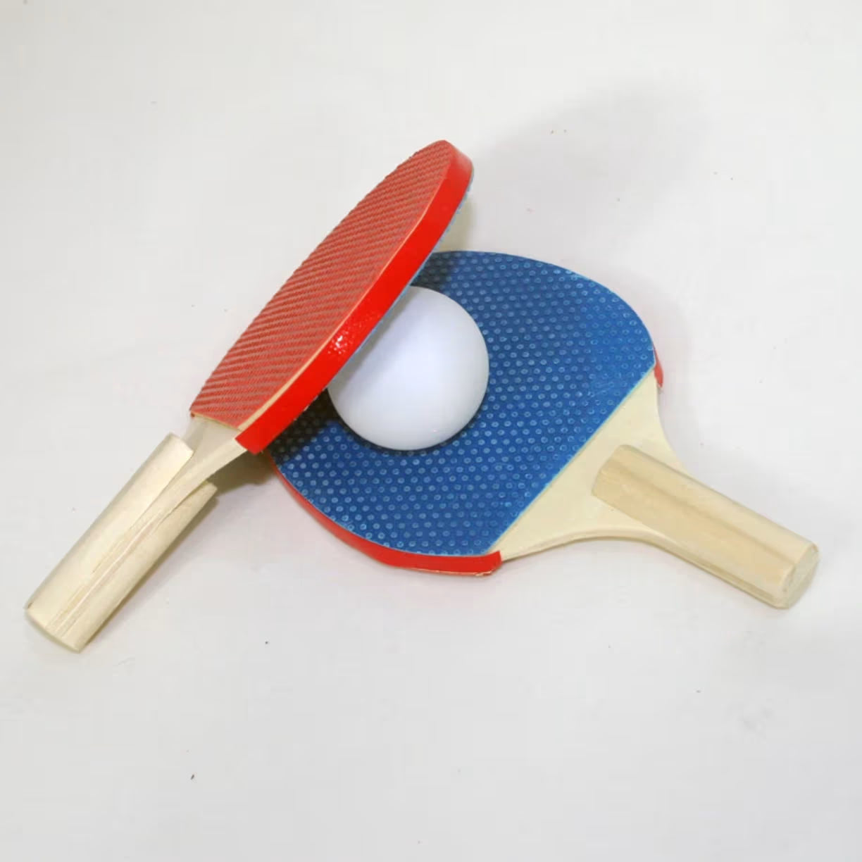 Krupni plan dva mala reketa za stoni tenis u plavoj i crvenoj boji sa belom lopticom