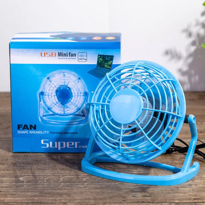 Svetlo plavi plasticni mini ventilator sa usb kablom pored plave fabricke kutije na drvenom stolu