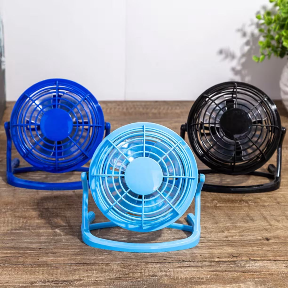 Tri mini stona ventilatora u tamno plavoj svetlo plavoj i crnoj boji poredjani na drvenoj povrsini