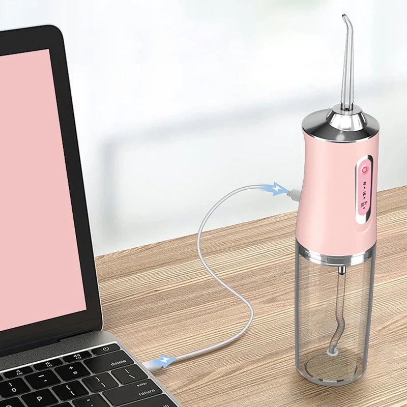 Roze oralni tus za zube povezan USB kablom na laptop tokom punjenja