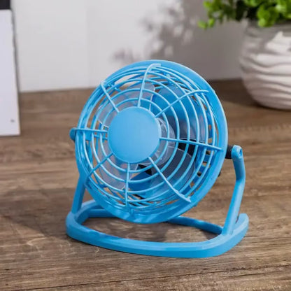 Svetlo plavi mini ventilator sa plasticnim propelerima slikan izbliza na stolu pored saksije