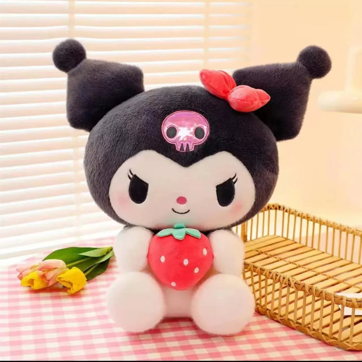 Plisana igracka Kuromi sa crvenom jagodom na roze kariranom stolu