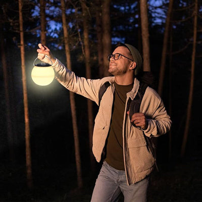 Muskarac drzi upaljenu lampu u sumi tokom noci, prikazuje njenu prenosivost i upotrebljivost za planinarenje.