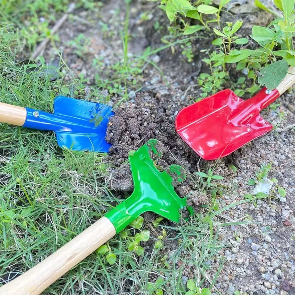 Tri sarena rucna alata zabodena u crnu zemlju i travu tokom uredjenja baste