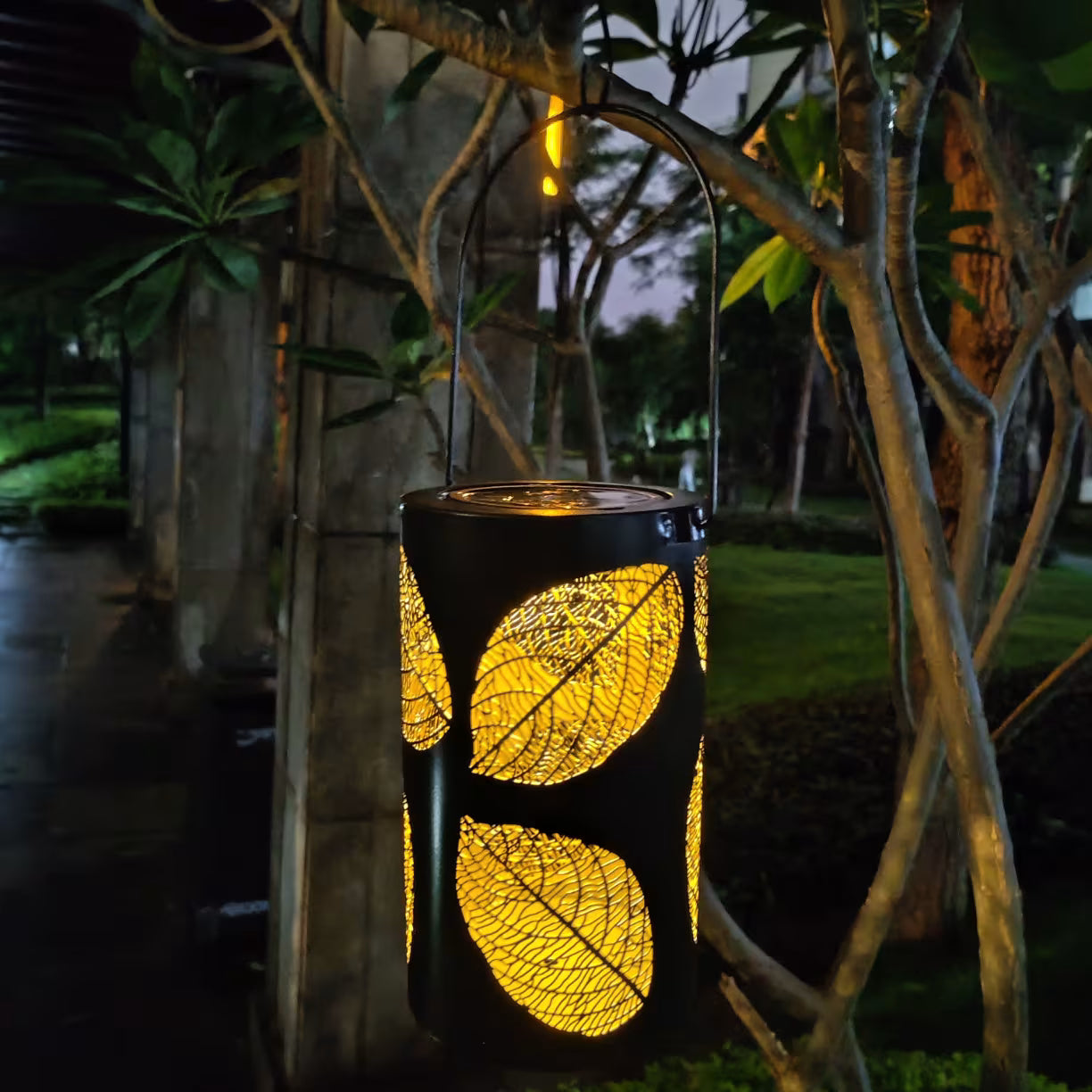 Solarna LED lampa sa motivom listova okacena u basti tokom noci