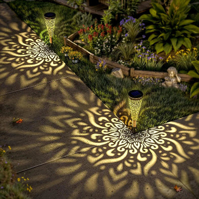 Solarne bastenske lampe koje projektuju dekorativne sare na stazi, obasjavajuci ivicu travnjaka i stvarajuci magicnu atmosferu u dvoristu.