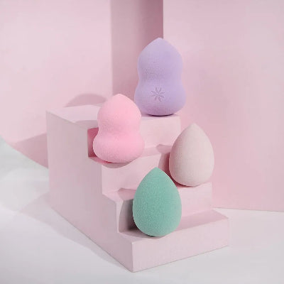 Set sundjera za sminku u raznim oblicima, prikazan na dekorativnom podijumu, u pastelnim bojama.