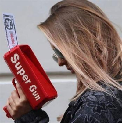 Zenska osoba drzi Super Gun pistolj za ispaljivanje novca. Igracka je lagana i laka za rukovanje, pogodna za koriscenje na svim vrstama proslava.