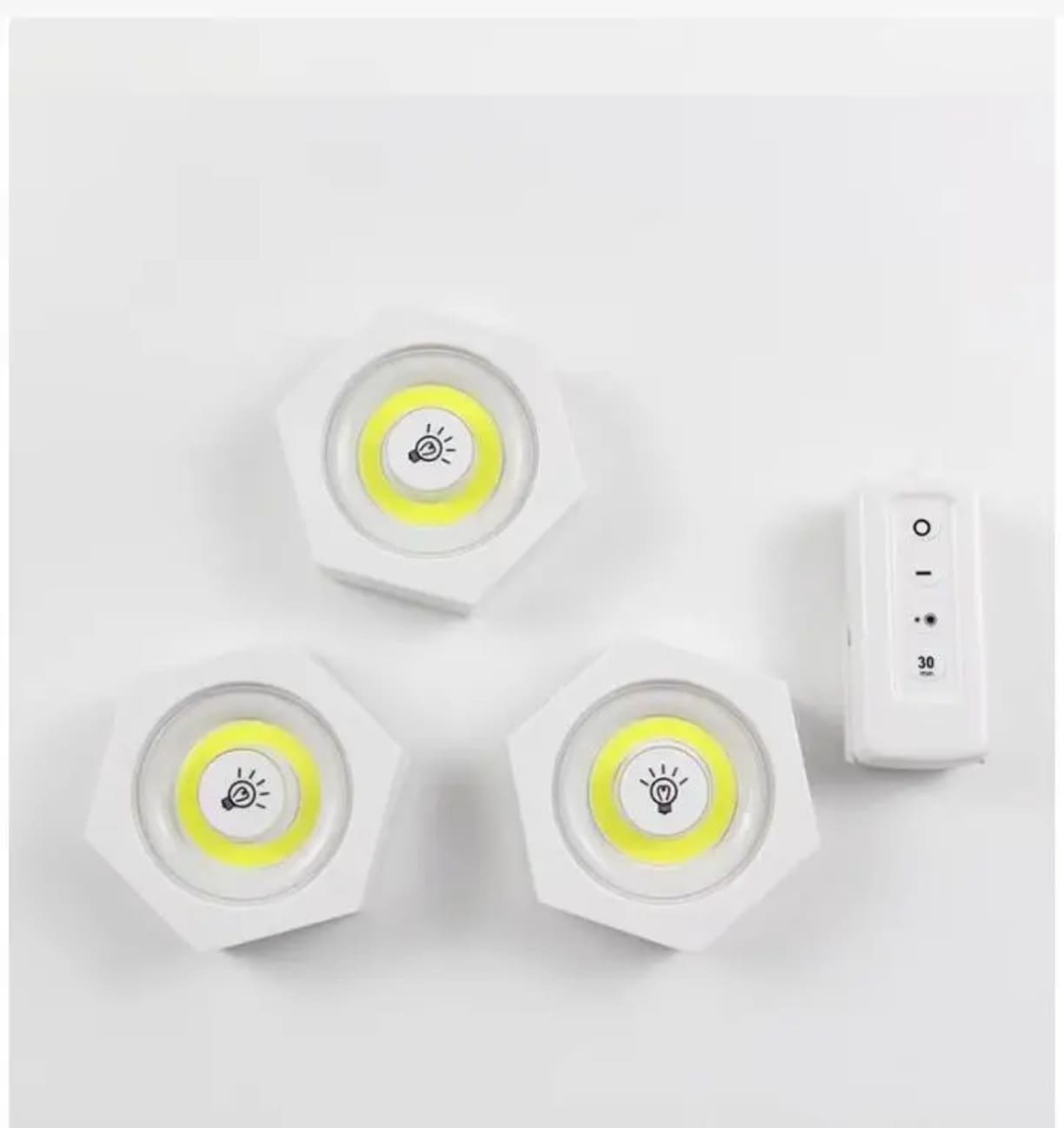 Komplet od tri bele bezicne lampe rasporedjene pored duguljastog daljinskog upravljaca sa oznakama za paljenje gasi i tajmer