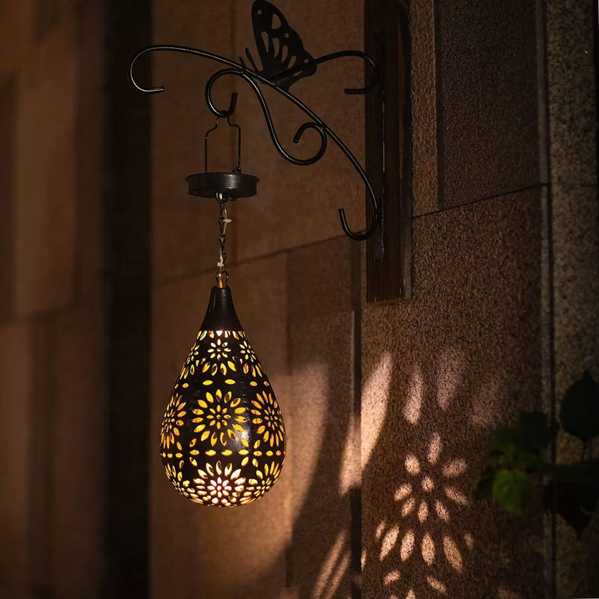 Solarna lampa visi sa ukrasnog crnog zidnog nosaca sa motivom leptira i pravi senke na zidu kuce